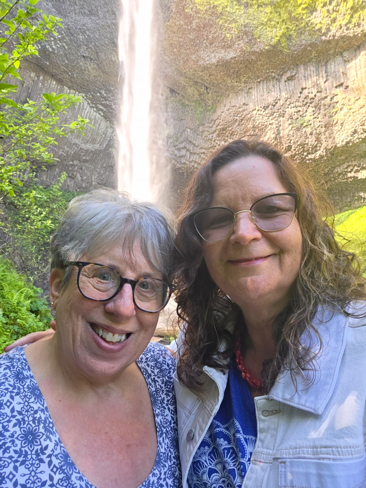 Two smiling A Great Oregon Wine Tour guides photographed in front of Latourell Falls and its columnar basalt cliff in the Columbia River Gorge